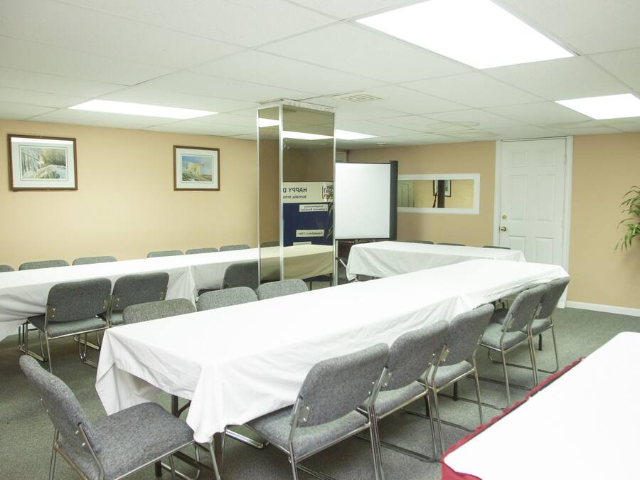 A conference room with long tables and chairs, a whiteboard, framed pictures on the wall, and a door.