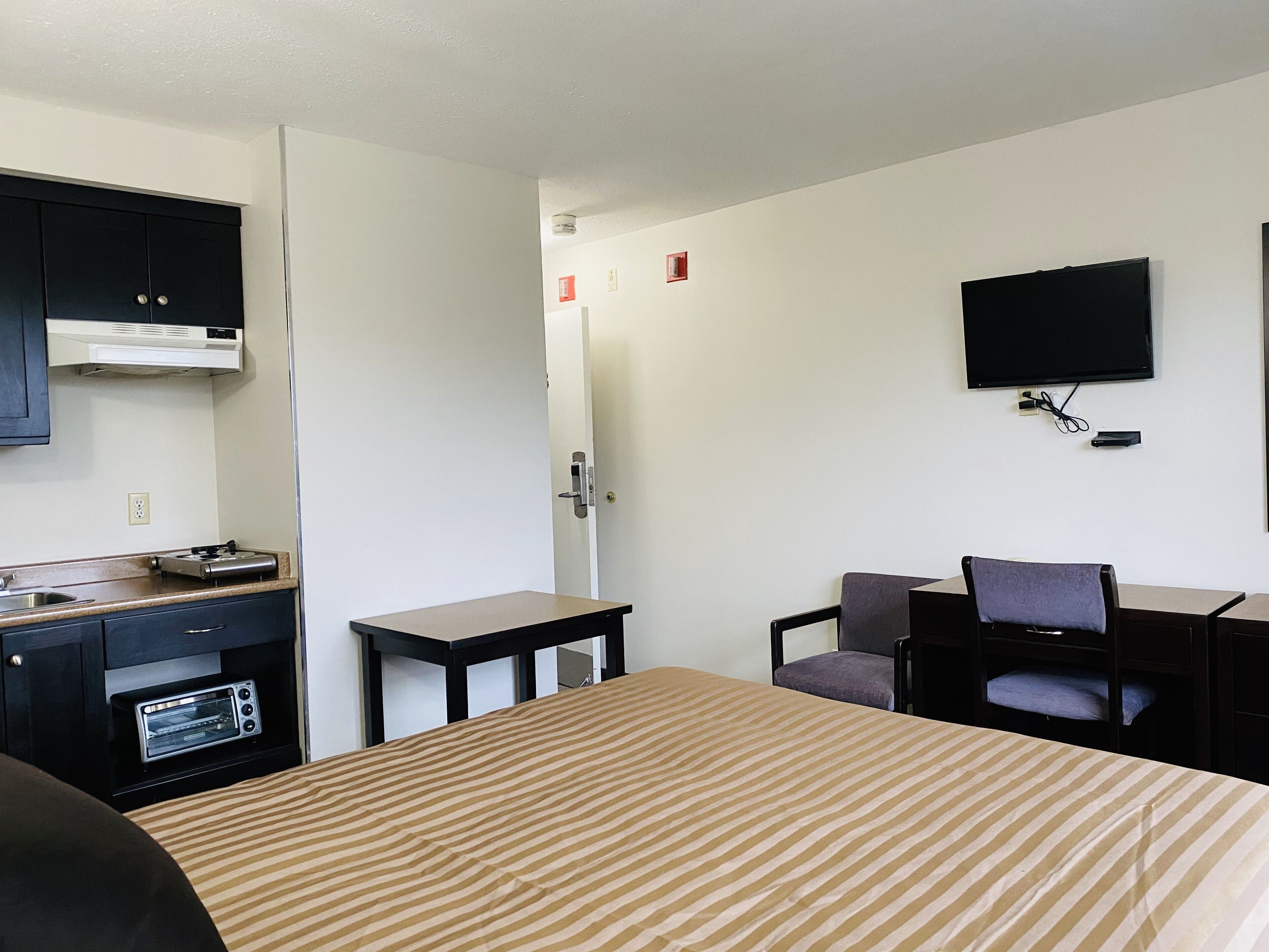 Ein Hotelzimmer mit Bett, Schreibtisch, Stuhl, Fernseher und einer Küchenzeile mit Herd und Backofen.