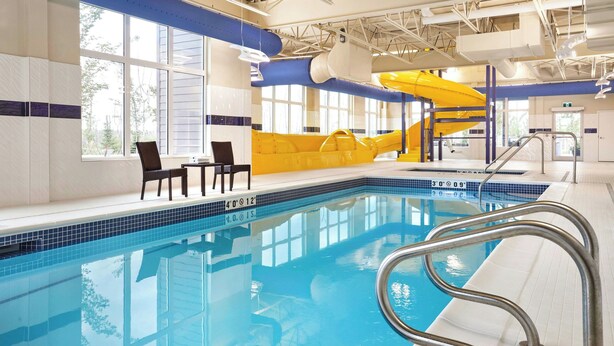 Une piscine intérieure avec un toboggan jaune, un espace détente et une barrière transparente autour de la piscine.