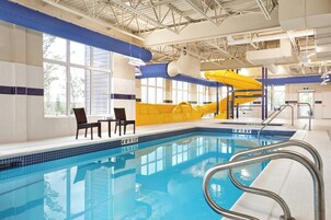 Una piscina interior con un tobogán amarillo, zona de estar y barandilla visible junto a la piscina.