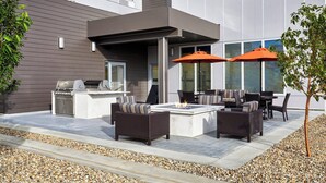Une terrasse extérieure équipée d’un barbecue, d’un espace salon et de parasols.