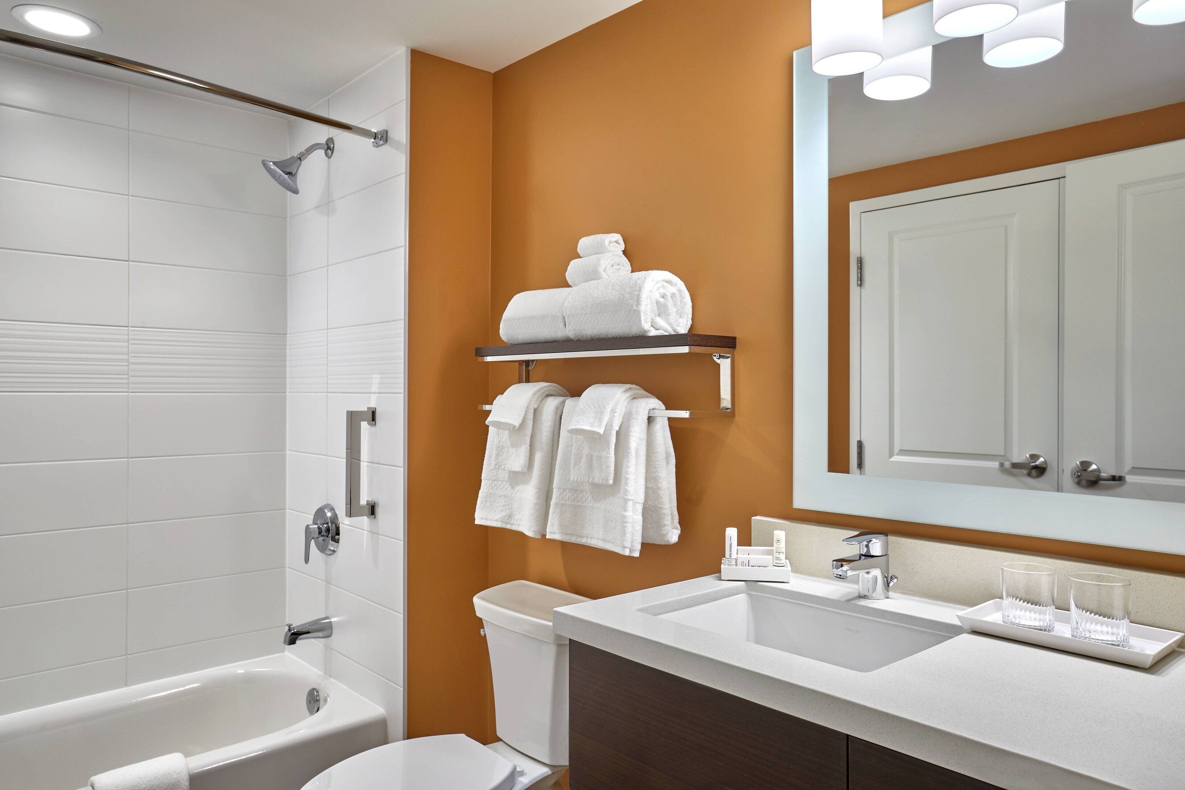 Un baño moderno con bañera, inodoro y lavamanos. Hay un perchero con toallas y un espejo sobre el lavamanos.