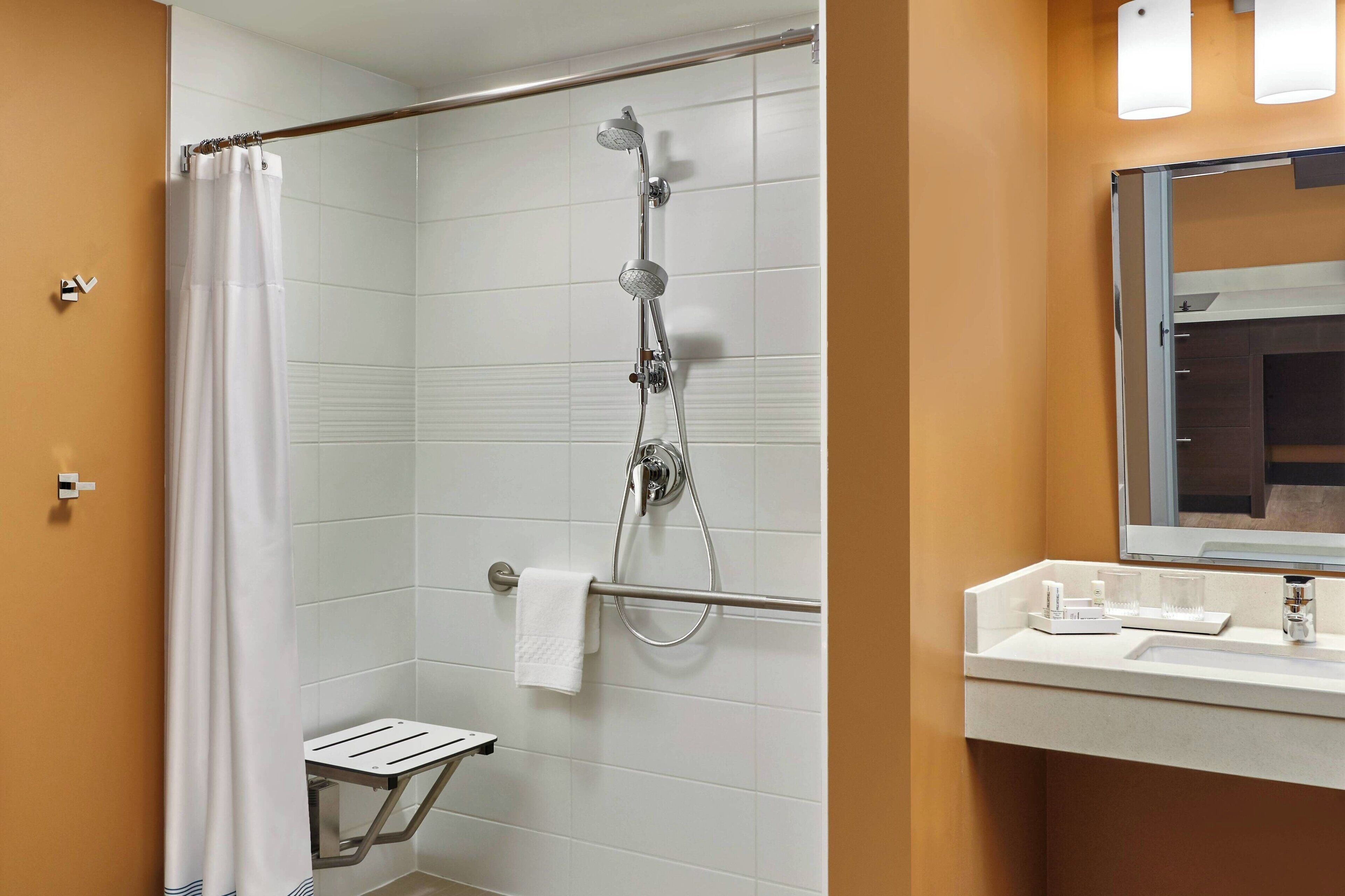 Ein Badezimmer mit Dusche, Handtuchhalter, Waschbecken mit Pflegeprodukten und einem Spiegel.