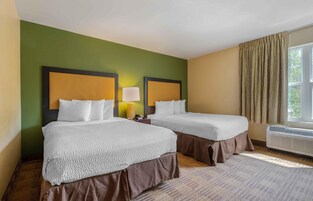 Quarto de hotel com duas camas, uma janela com cortinas e um ar condicionado fixado na parede.