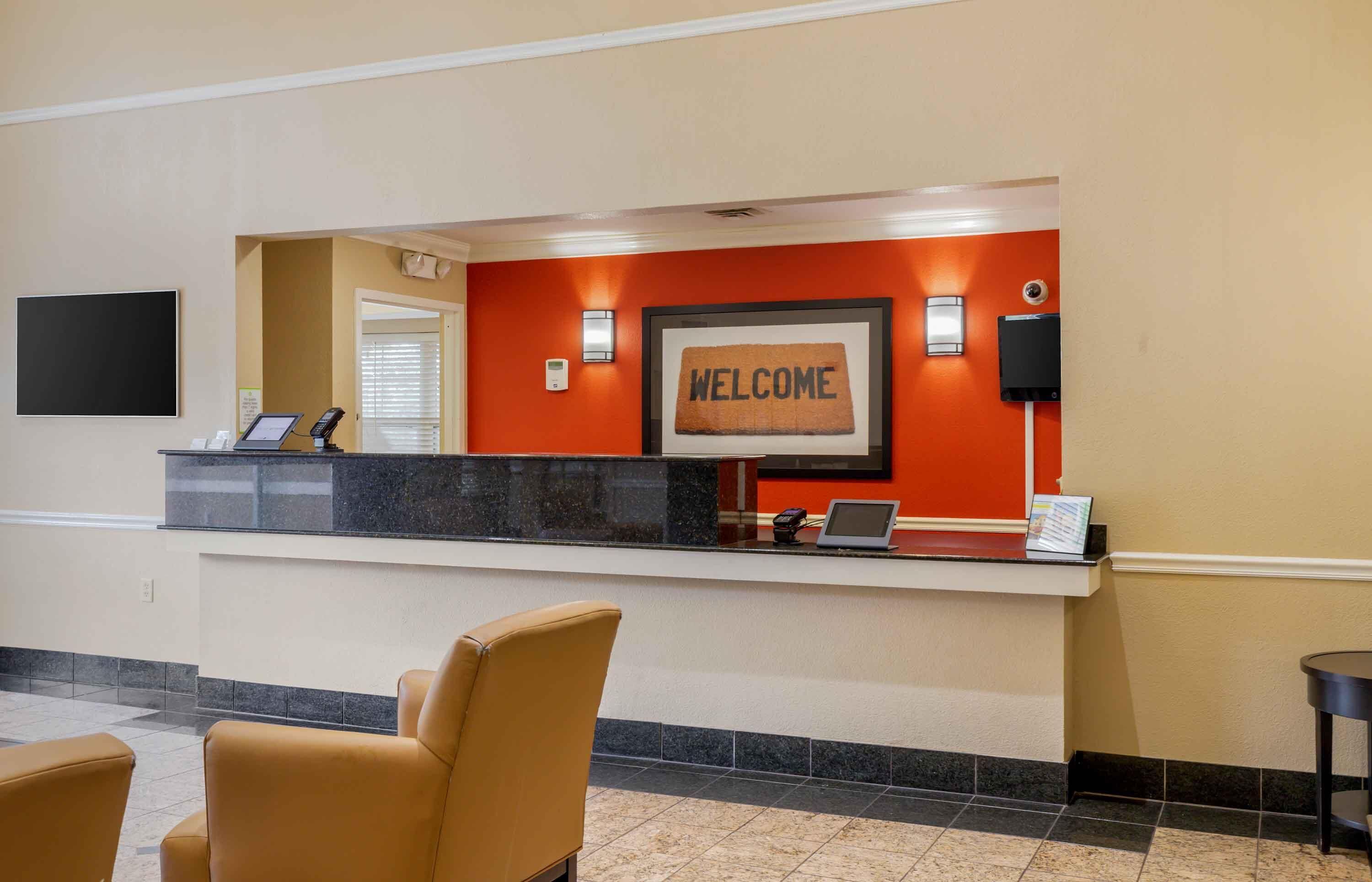 Una recepción de hotel con un cartel de 'WELCOME', una pantalla digital y una cámara de seguridad.
