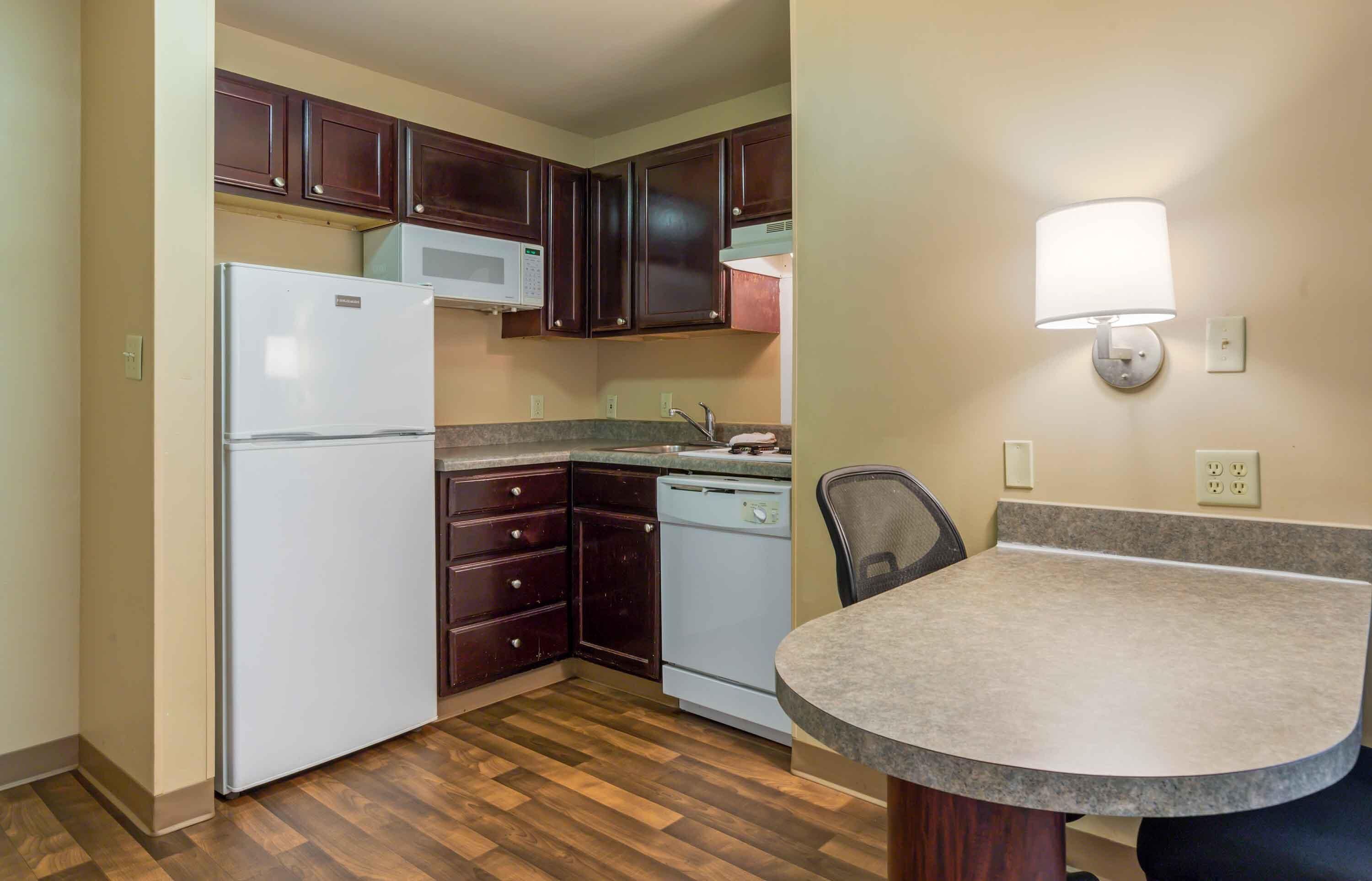 A compact kitchen with a refrigerator, microwave, dishwasher, and a dining area with a table and chair.