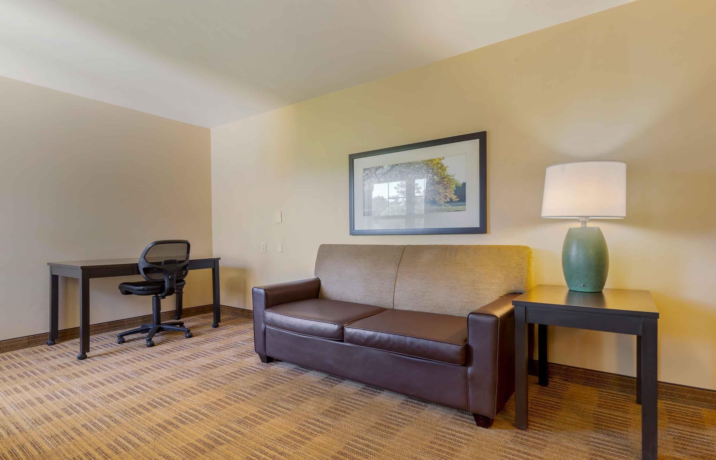 Habitación de hotel con un sofá de cuero marrón, un escritorio pequeño con una silla, una lámpara y un cuadro en la pared.