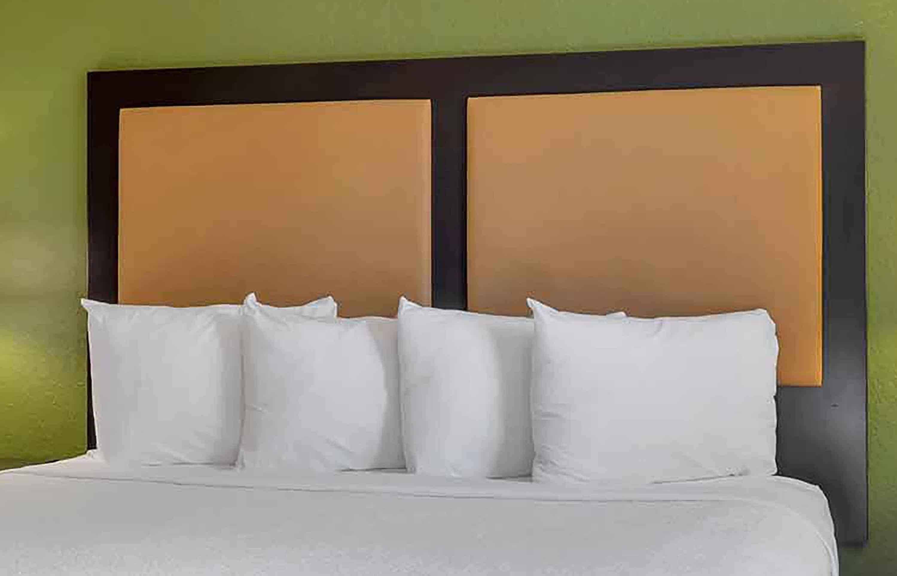 Una cama con ropa de cama y almohadas blancas, un cabecero oscuro y una pared verde.