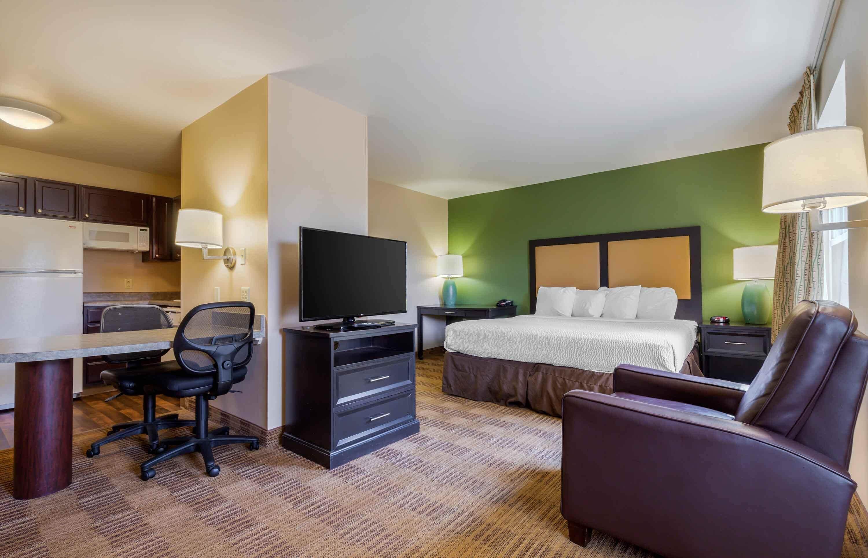 A hotel room with a bed, desk, chair, television, and a green accent wall.
