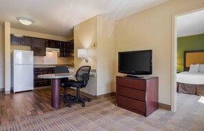 Een compacte hotelkamer met kitchenette, bureau met stoel, televisie en bed.