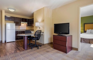 Habitación de hotel compacta con kitchenette, escritorio, silla, televisor y cama.