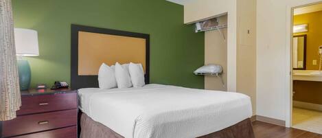 Une chambre d’hôtel avec un lit, une commode, un miroir et une salle de bain visible à travers une porte ouverte.