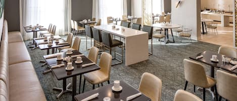Un comedor de hotel con varias mesas y sillas, una larga barra y una cocina al fondo.