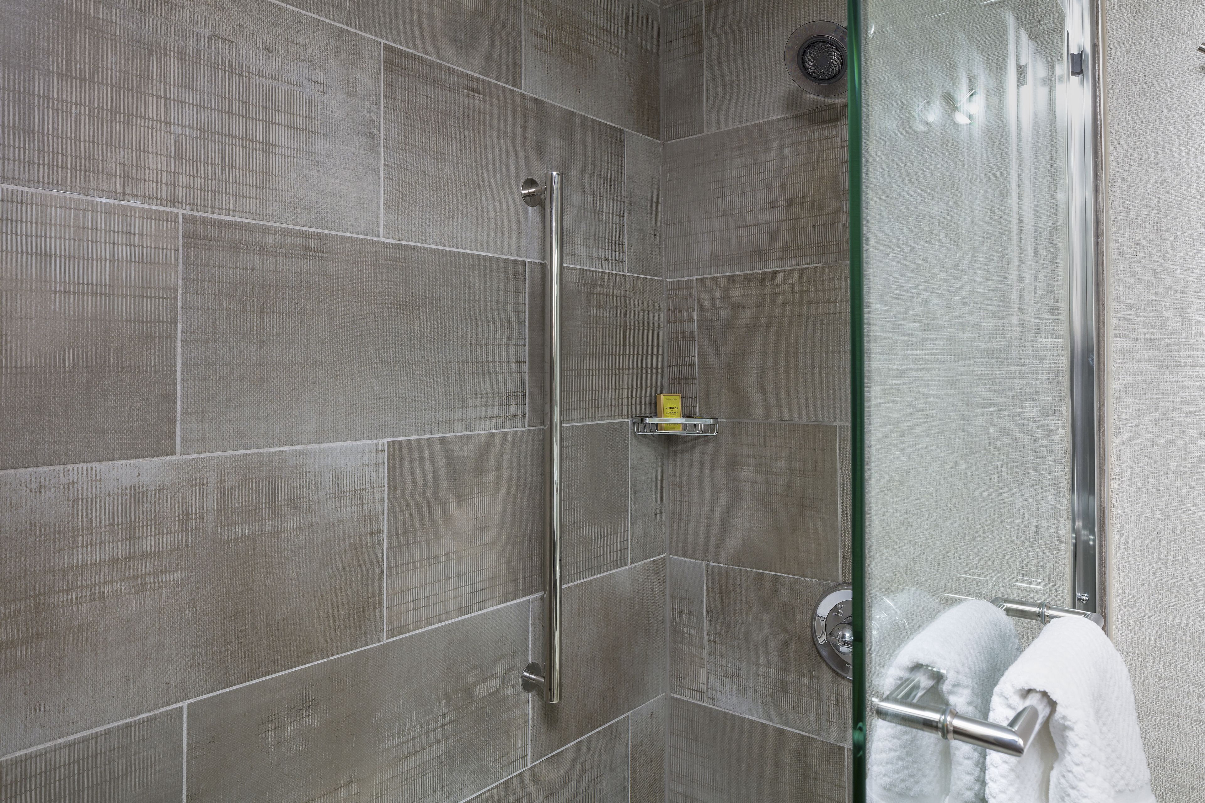 A shower with a glass door, a handrail, and a towel rack.