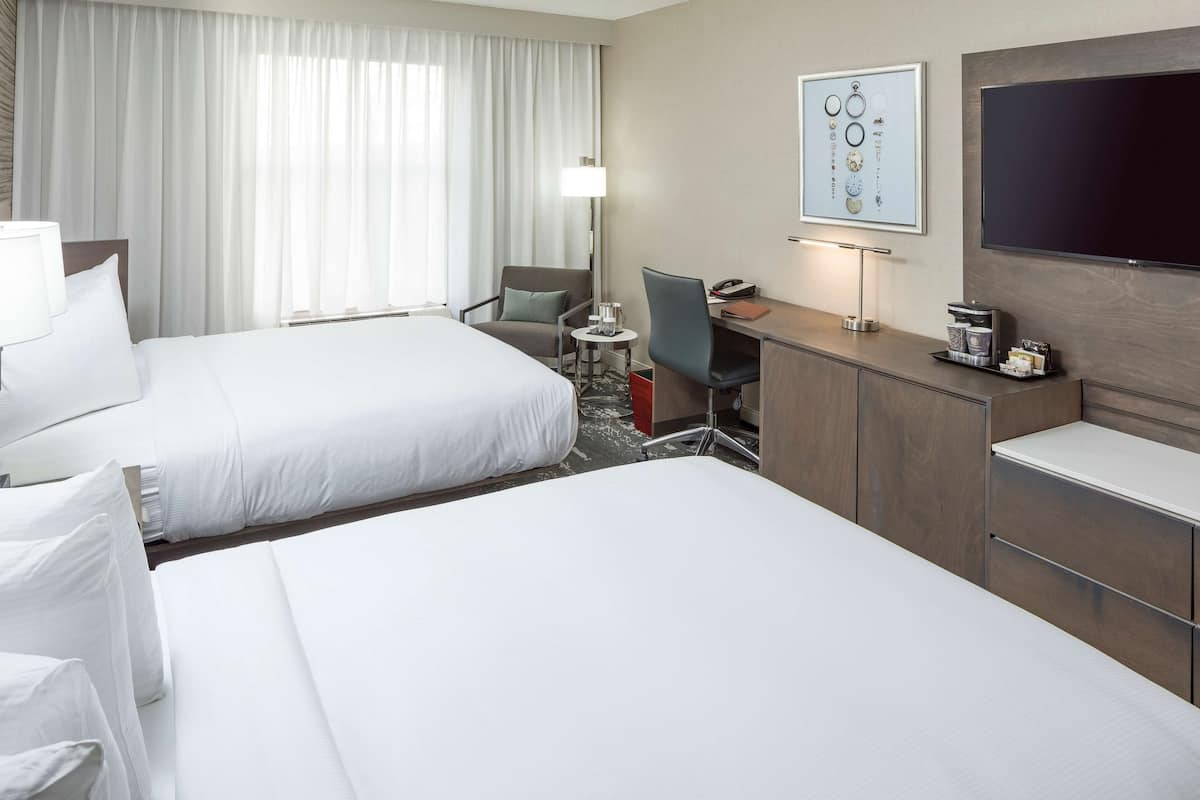 Ett hotellrum med två sängar, ett skrivbord, en stol, en TV och ett fönster med gardiner.