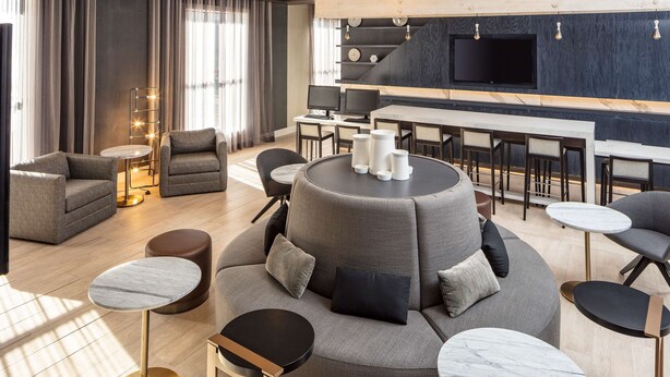 A modern lounge area with sofas, round tables, and a bar with multiple seating options.