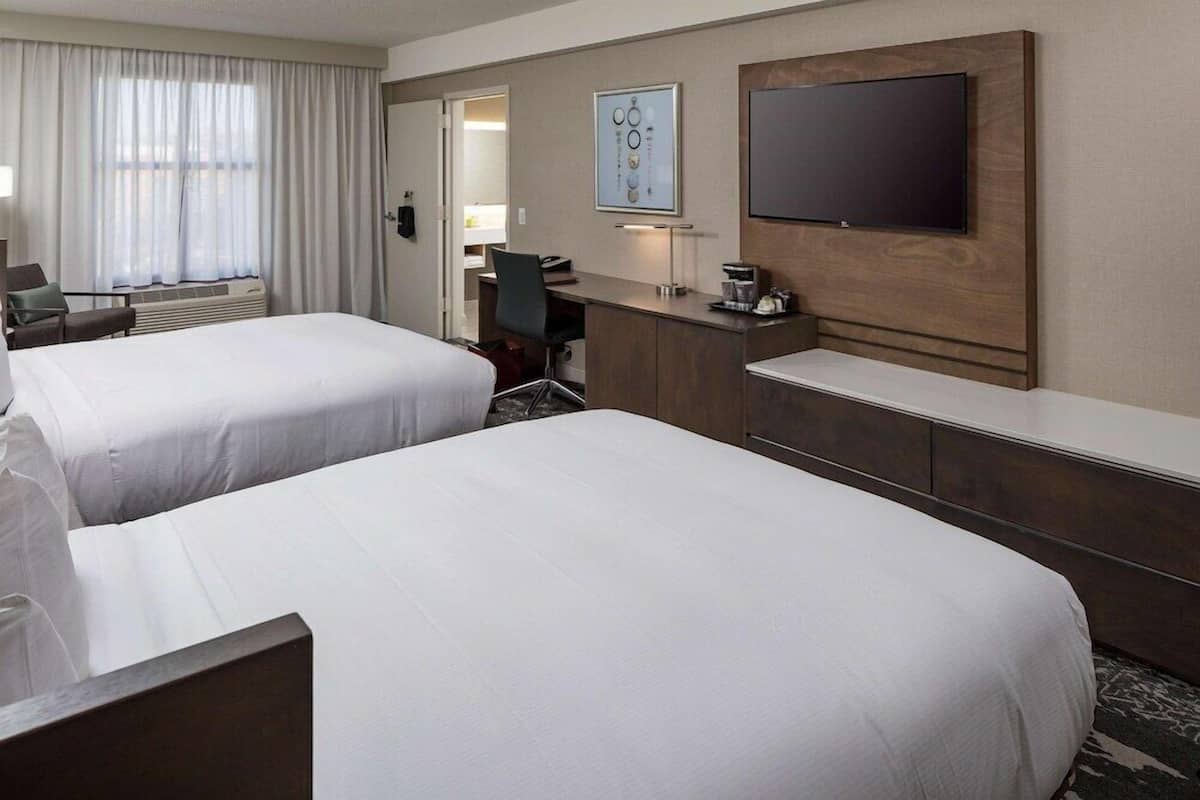 Ett hotellrum med två sängar, ett skrivbord, en stol, en TV och en kaffebryggare.