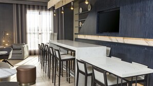 A modern kitchen with a marble countertop, bar stools, and a flat-screen TV mounted on the wall.