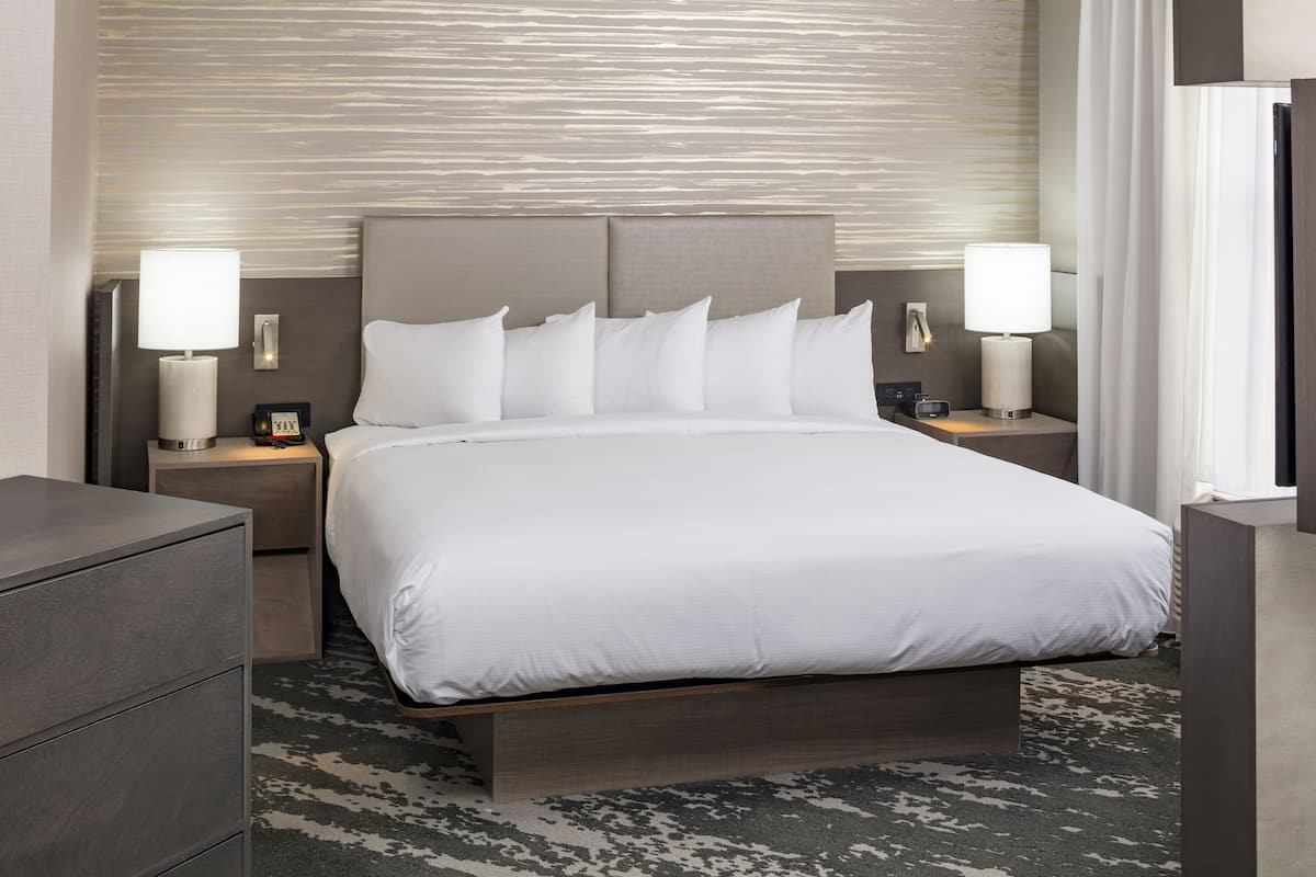 Ett modernt hotellrum med en stor säng, två sängbord med lampor, en byrå i trä och en mönstrad matta.
