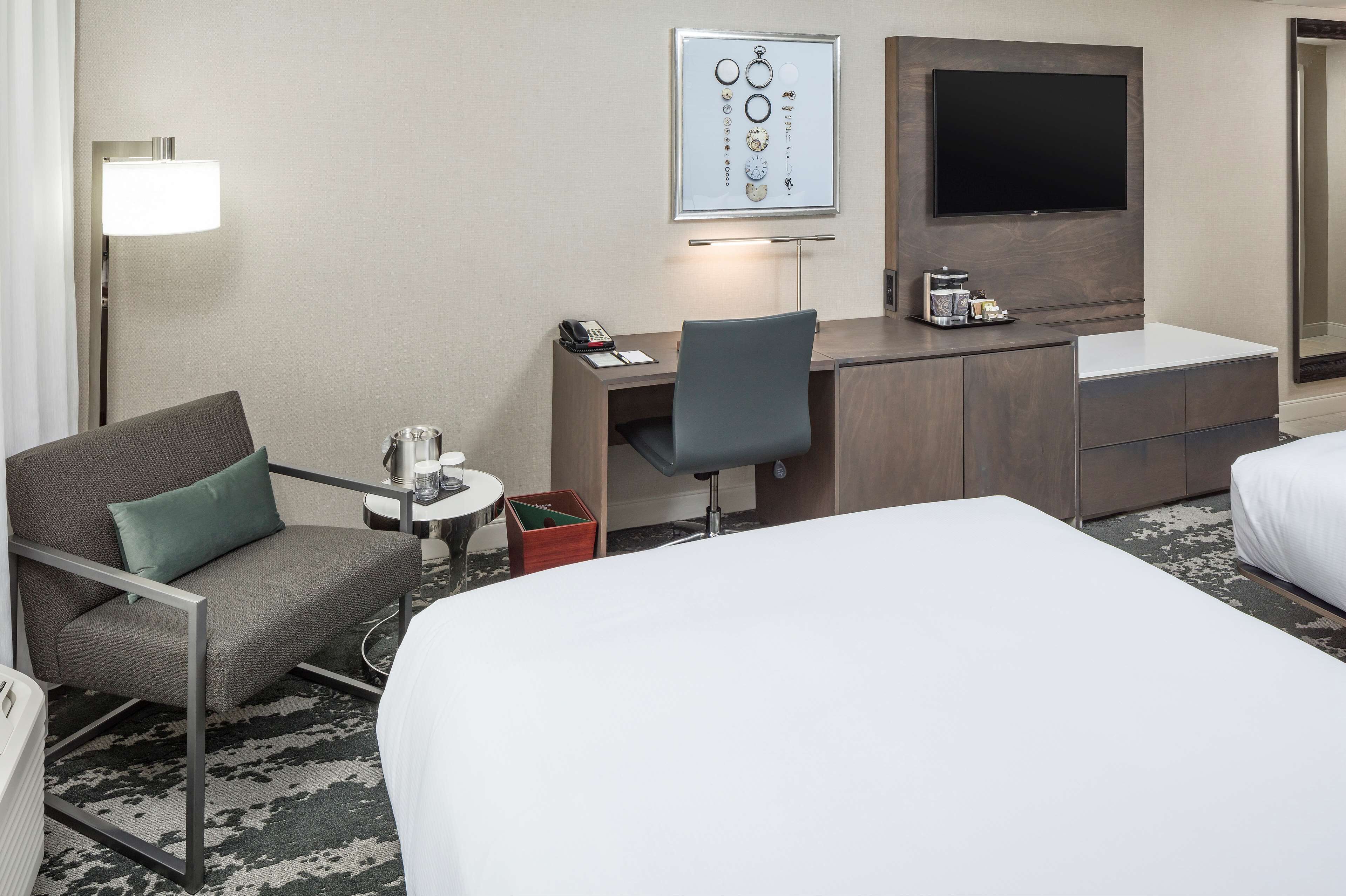A hotel room with a bed, a desk with a chair, a TV, and a lamp.