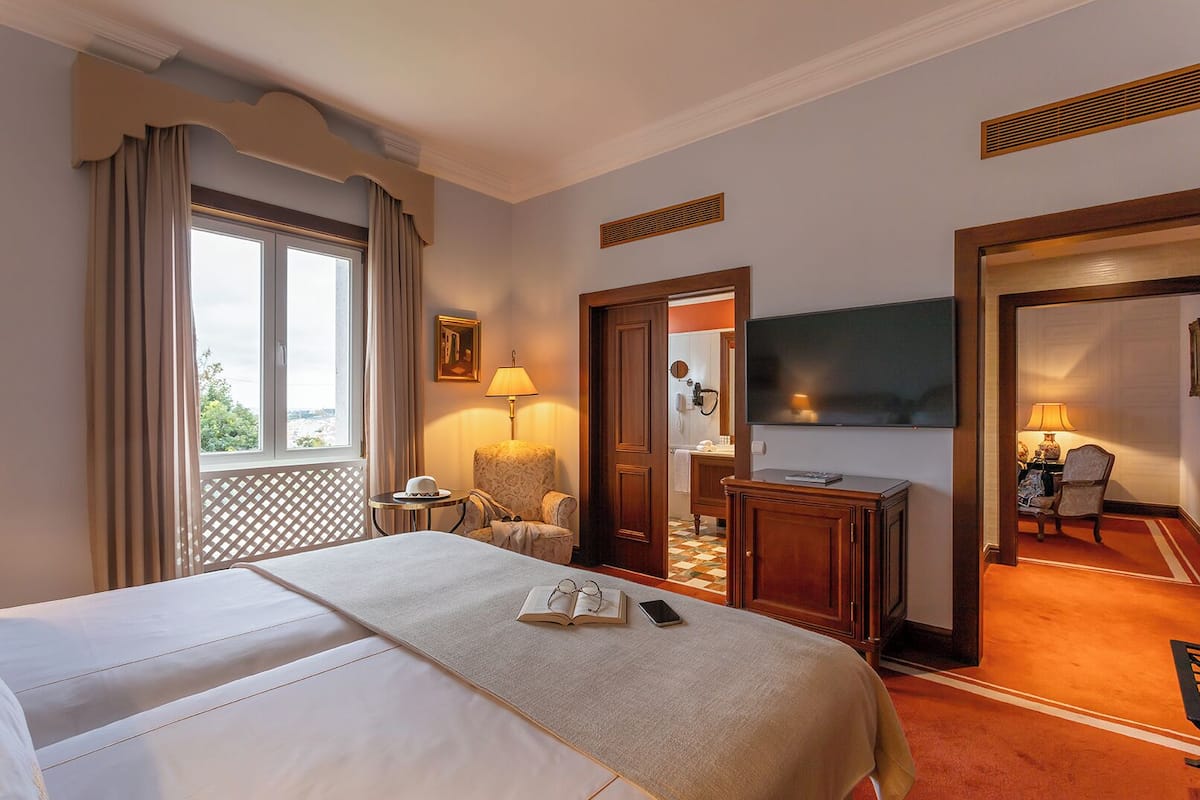 Une chambre d’hôtel avec un grand lit, un bureau avec une lampe, une télévision et une vue sur la ville par la fenêtre.