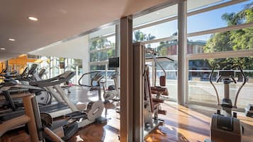 A gym with cardio machines, weight equipment, and large windows offering a view of the outdoors.