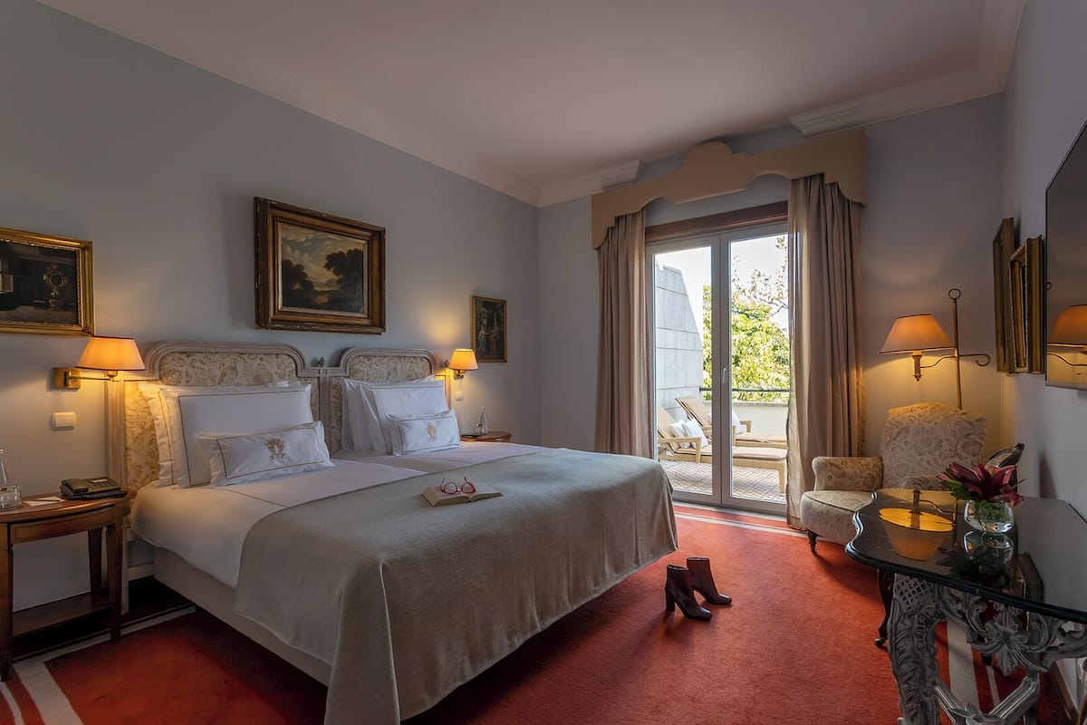 Une chambre d’hôtel avec un grand lit, deux tables de chevet, une table basse en verre, une chaise et un balcon avec vue.