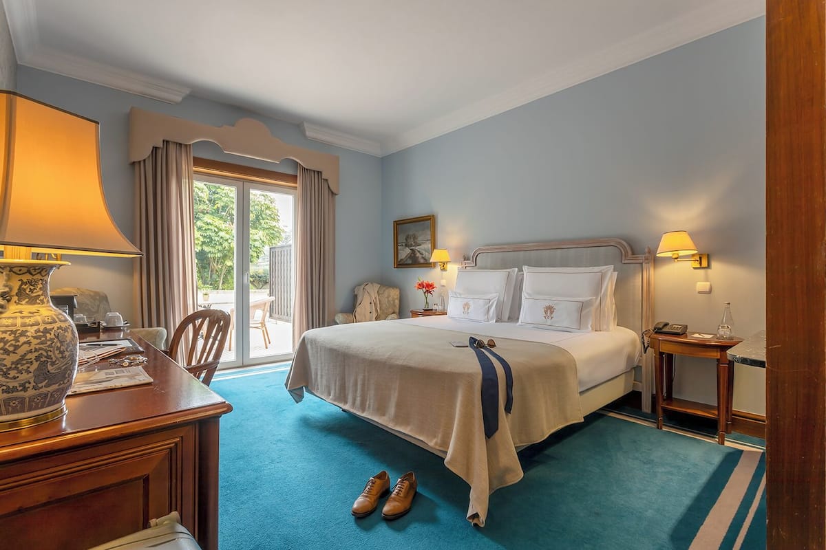 Une chambre d’hôtel avec un grand lit, un bureau avec une lampe, une chaise et une vue sur l’extérieur grâce à une porte coulissante.