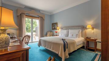 A hotel room with a large bed, a desk with a lamp, a chair, and a view of the outdoors through a sliding door.