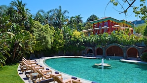A pool with lounge chairs, a fountain, and a building with red and yellow walls. -  Pestana Palace Lisboa Hotel & National Monument - The Leading Hotels of the World (Lisbon)
