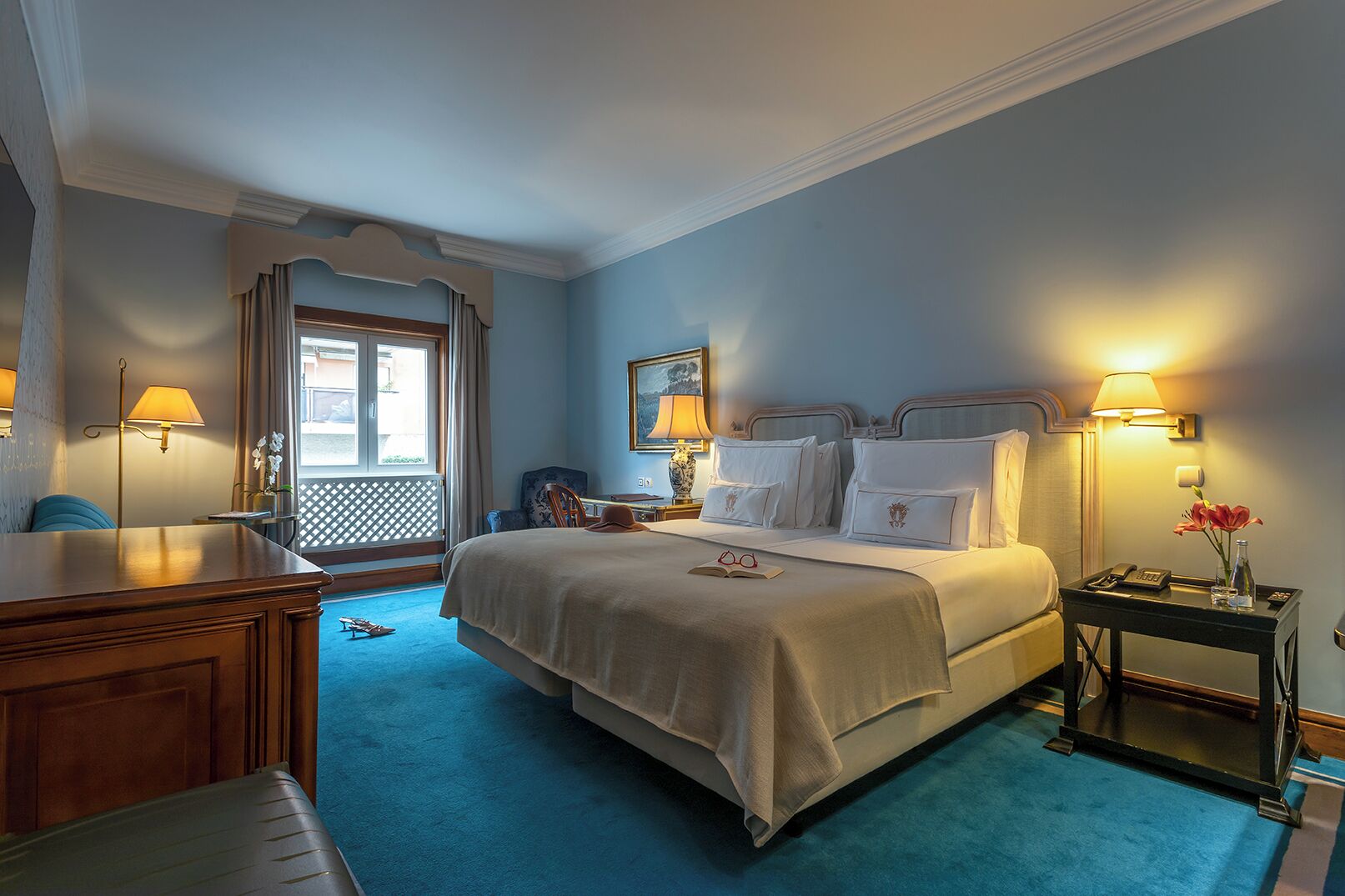 A hotel room with a large bed, a desk, a chair, a nightstand, and a window with curtains.