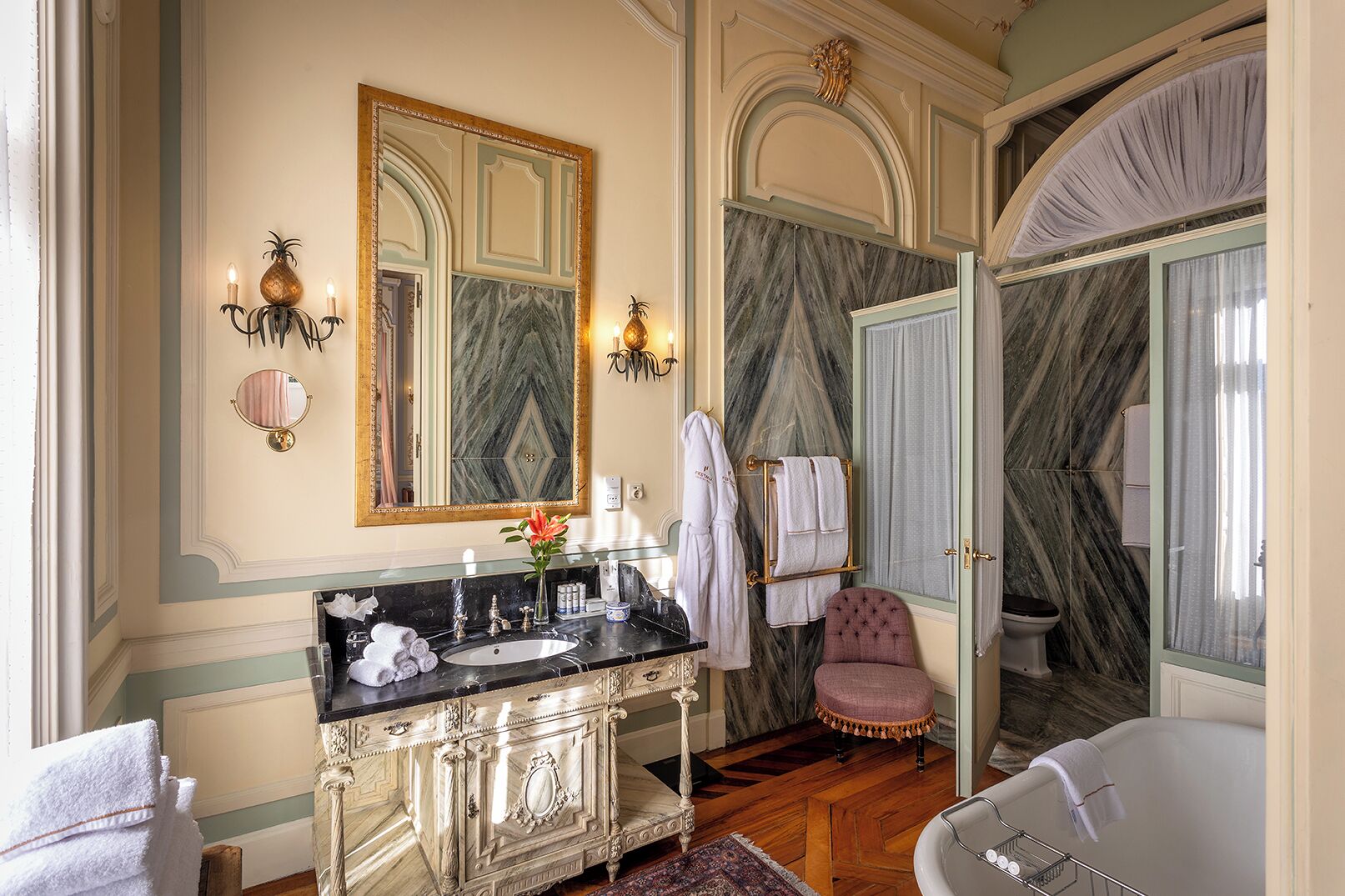 A luxurious bathroom with a marble vanity, a large mirror, a bathtub, and a vanity chair.