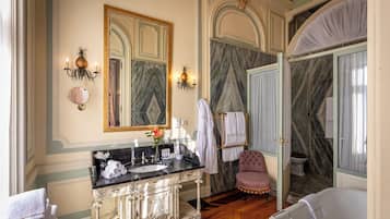 A luxurious bathroom with a marble vanity, a large mirror, a bathtub, and a vanity chair.