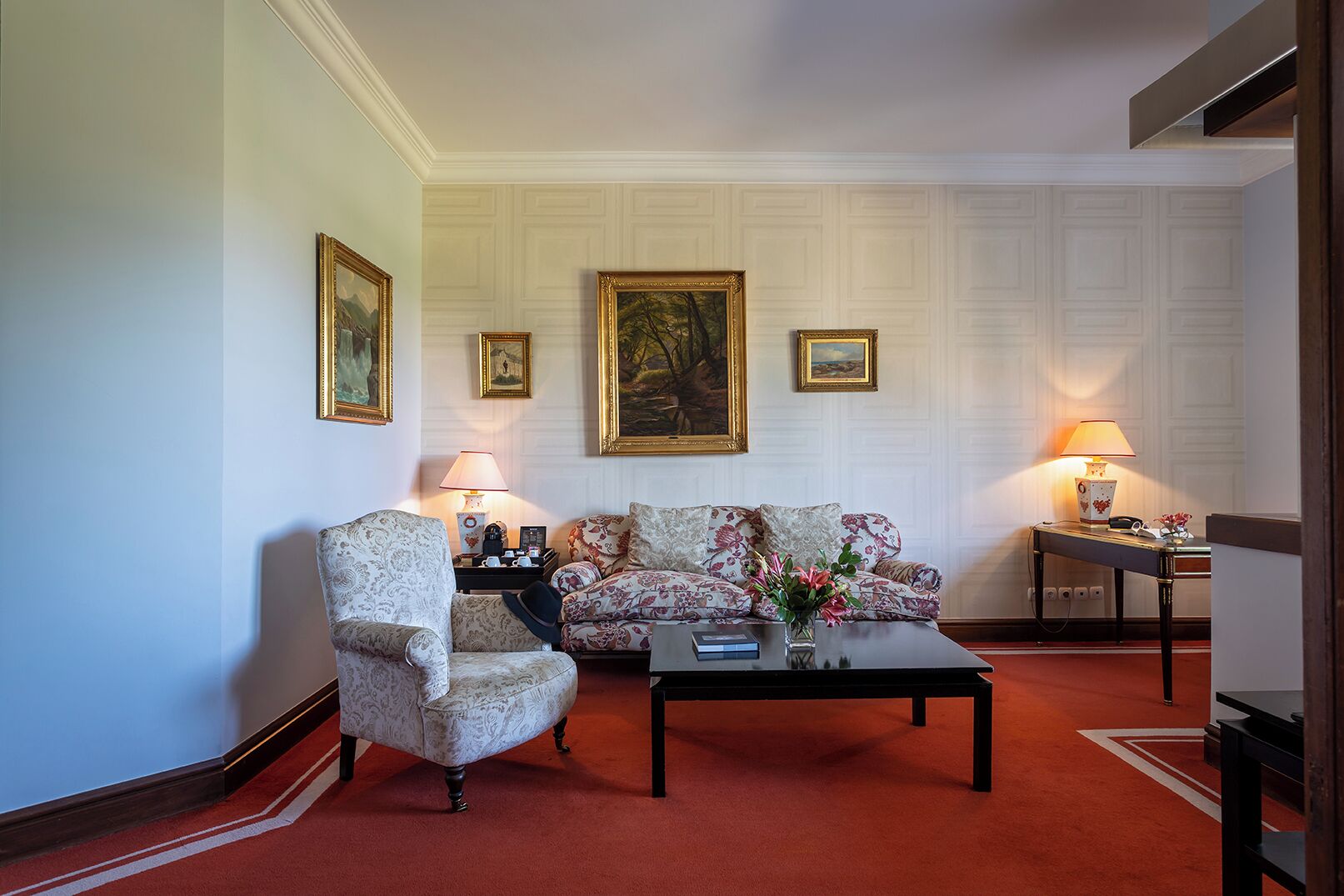 Una sala de estar con un sillón estampado, un sofá, una mesita de centro y dos lámparas.