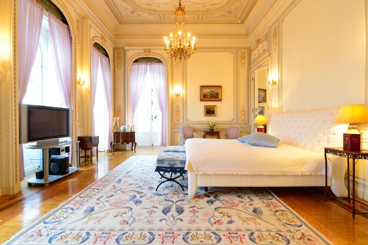 Une chambre spacieuse avec un grand lit, une télévision et un lustre.