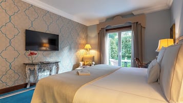Een hotelkamer met een groot bed, een aan de muur bevestigde televisie, een nachtkastje met een lamp en uitzicht op het omliggende landschap door een raam.