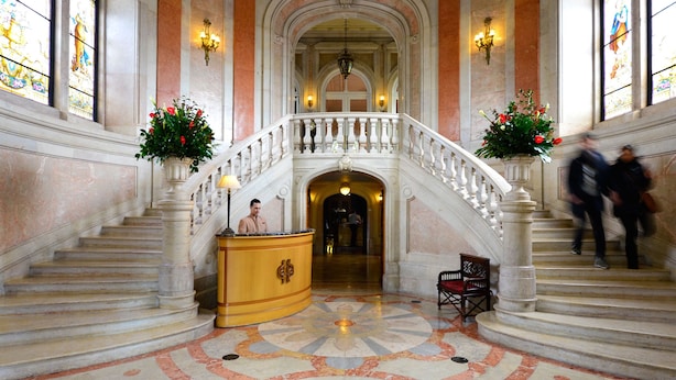 A grand staircase with a balustrade, a reception desk, and a bench. -  Pestana Palace Lisboa Hotel & National Monument - The Leading Hotels of the World (Lisbon)