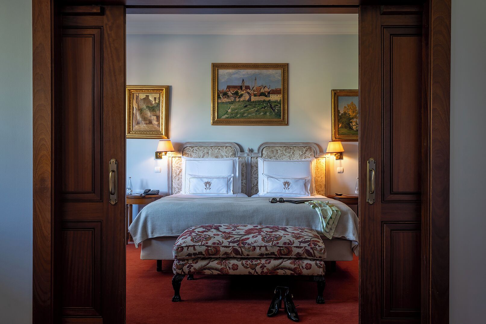A bedroom with a large bed, two bedside tables, a bench, and two wall-mounted lamps.