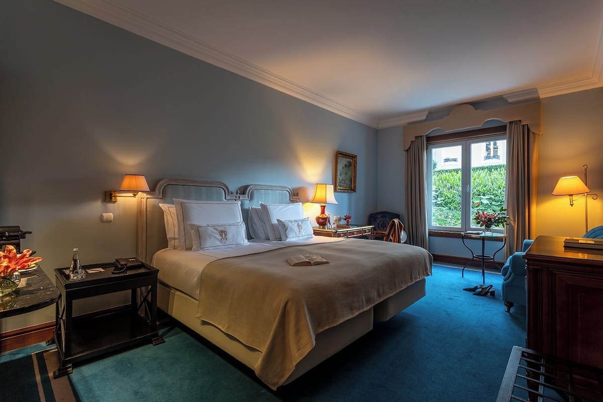Une chambre d’hôtel avec un grand lit, des lampes de chevet, un bureau et une vue sur la verdure.