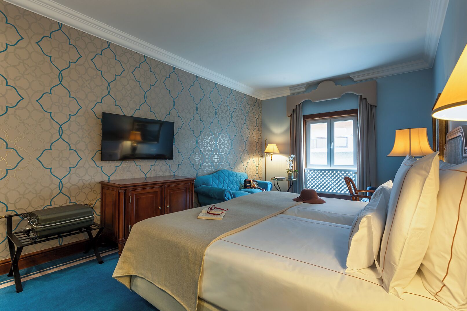 Et hotelværelse med en stor seng, et fjernsyn ophængt på væggen, et skrivebord med en lampe og udsigt til det fri gennem et vindue.