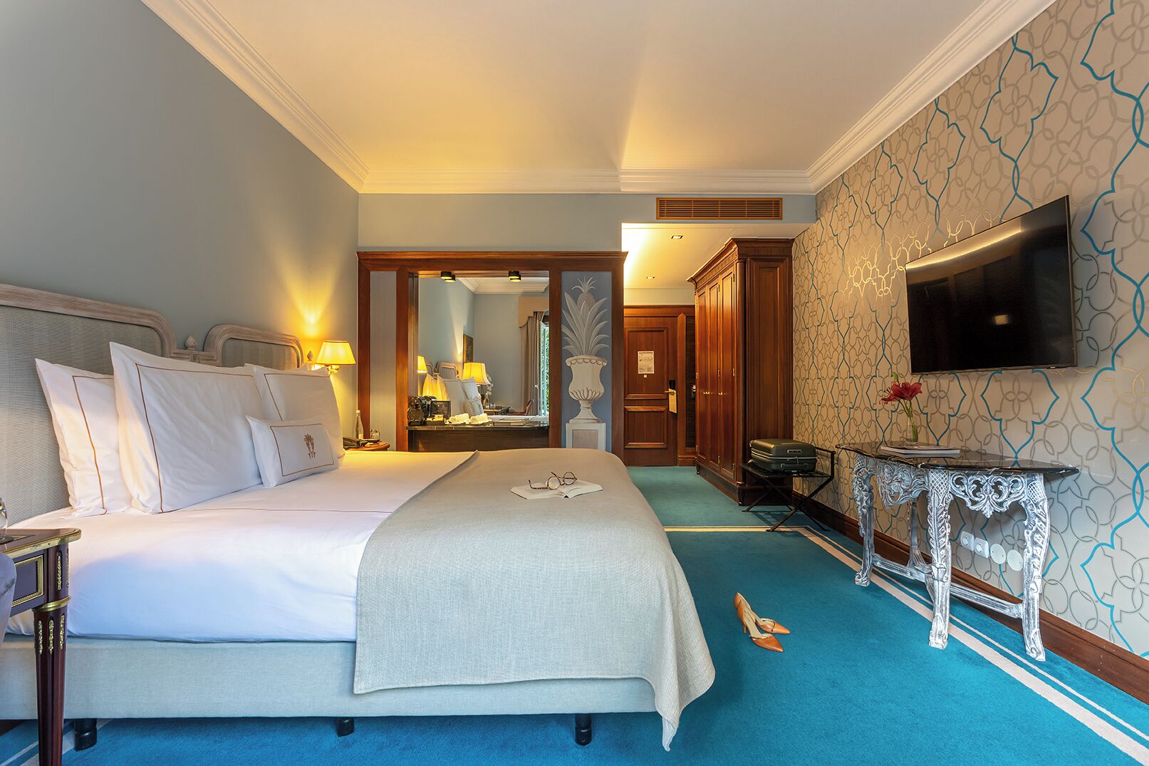 Una habitación de hotel con una cama grande, televisión, espejo y escritorio con silla.