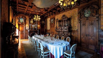 Ein formeller Speisesaal mit einem langen Tisch, gedeckt für eine Mahlzeit, umgeben von aufwendig gestalteten Holzwandverkleidungen und einer großen Chandelier.
