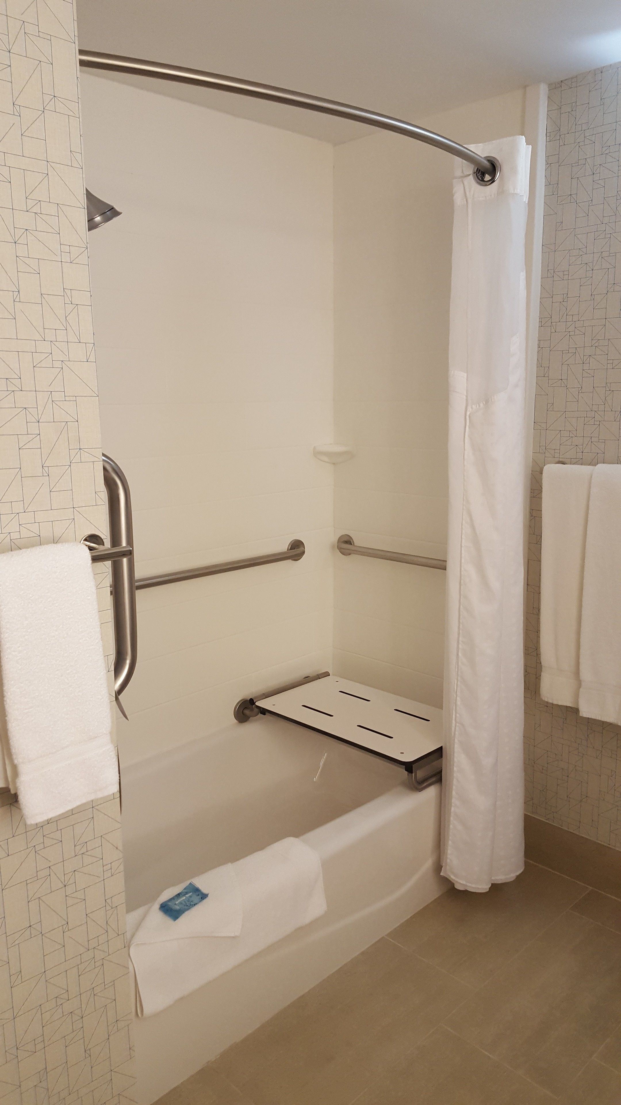 A shower area with a grab bar, a white shower curtain, and a towel rack.