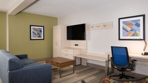 A modern hotel room with a sofa, a desk with a computer, a flat-screen TV, and two framed artworks on the wall. - Holiday Inn Express Louisville Northeast by IHG (Louisville)