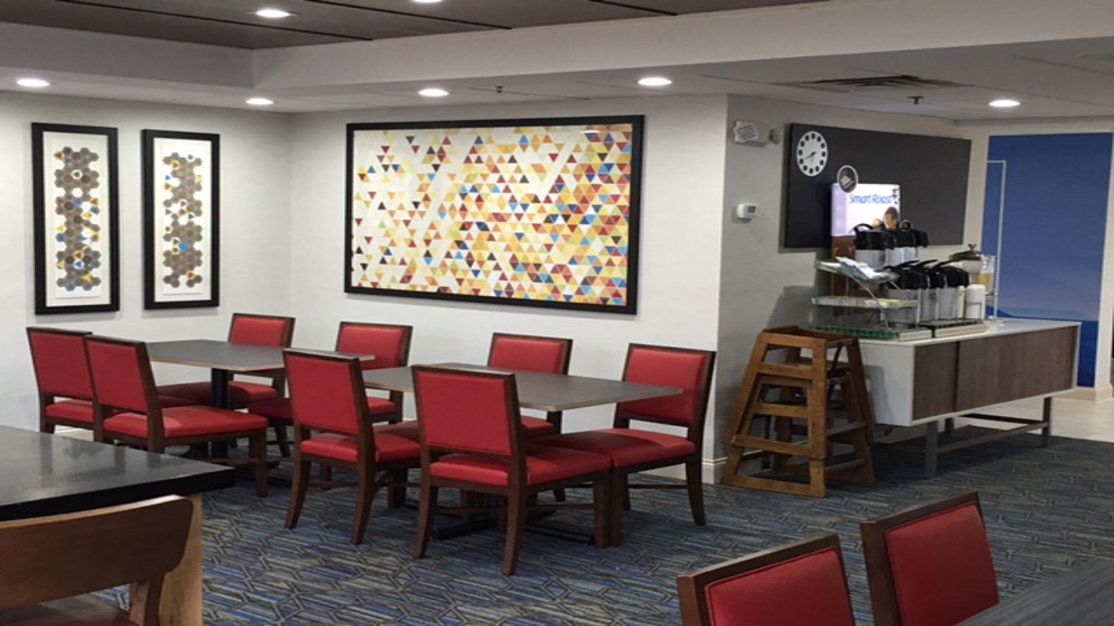 A conference room with a large table, red chairs, a coffee station, and a clock on the wall.