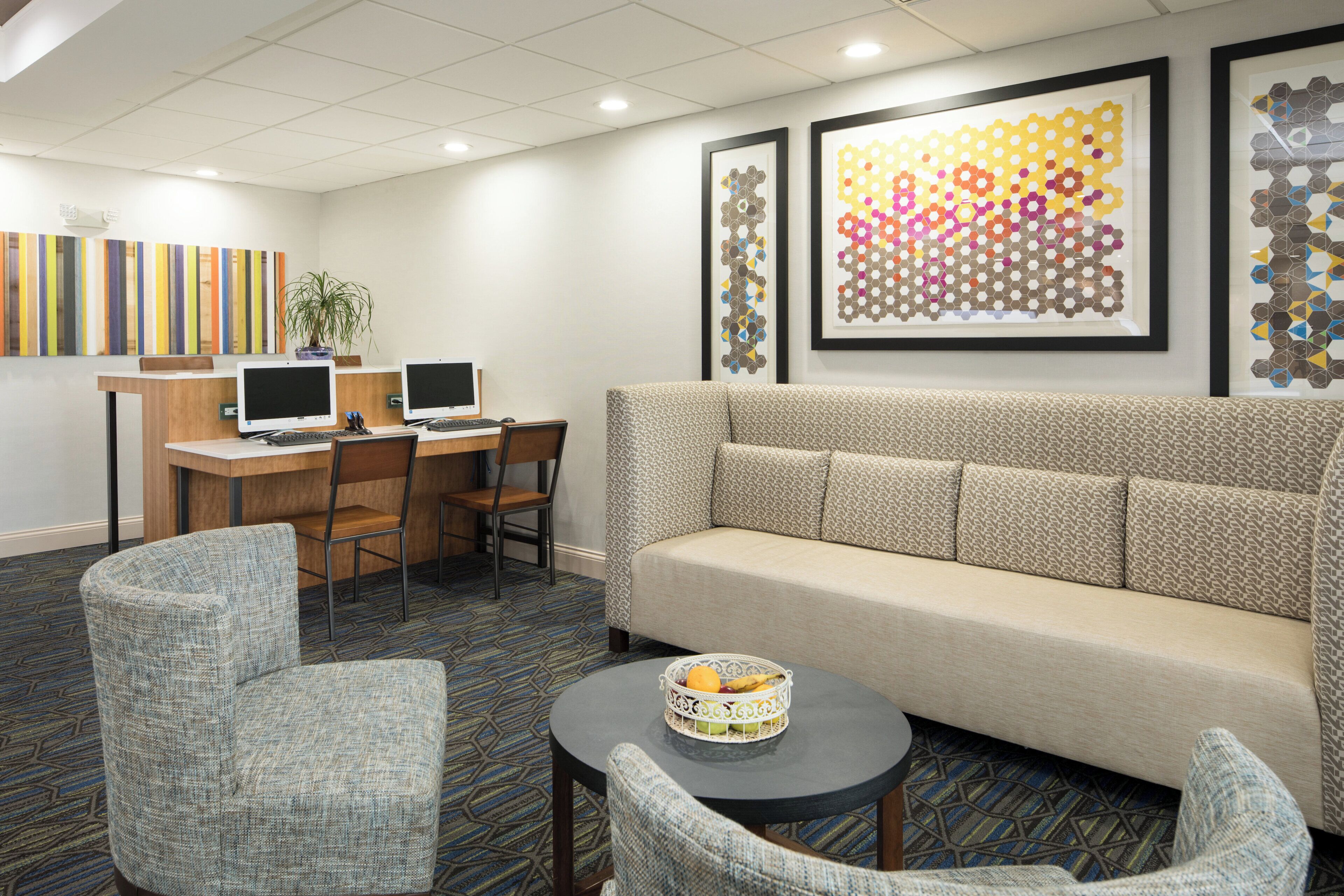 Un hall de hotel con un sofá, dos sillones, un escritorio con computadoras y obras de arte enmarcadas en la pared.