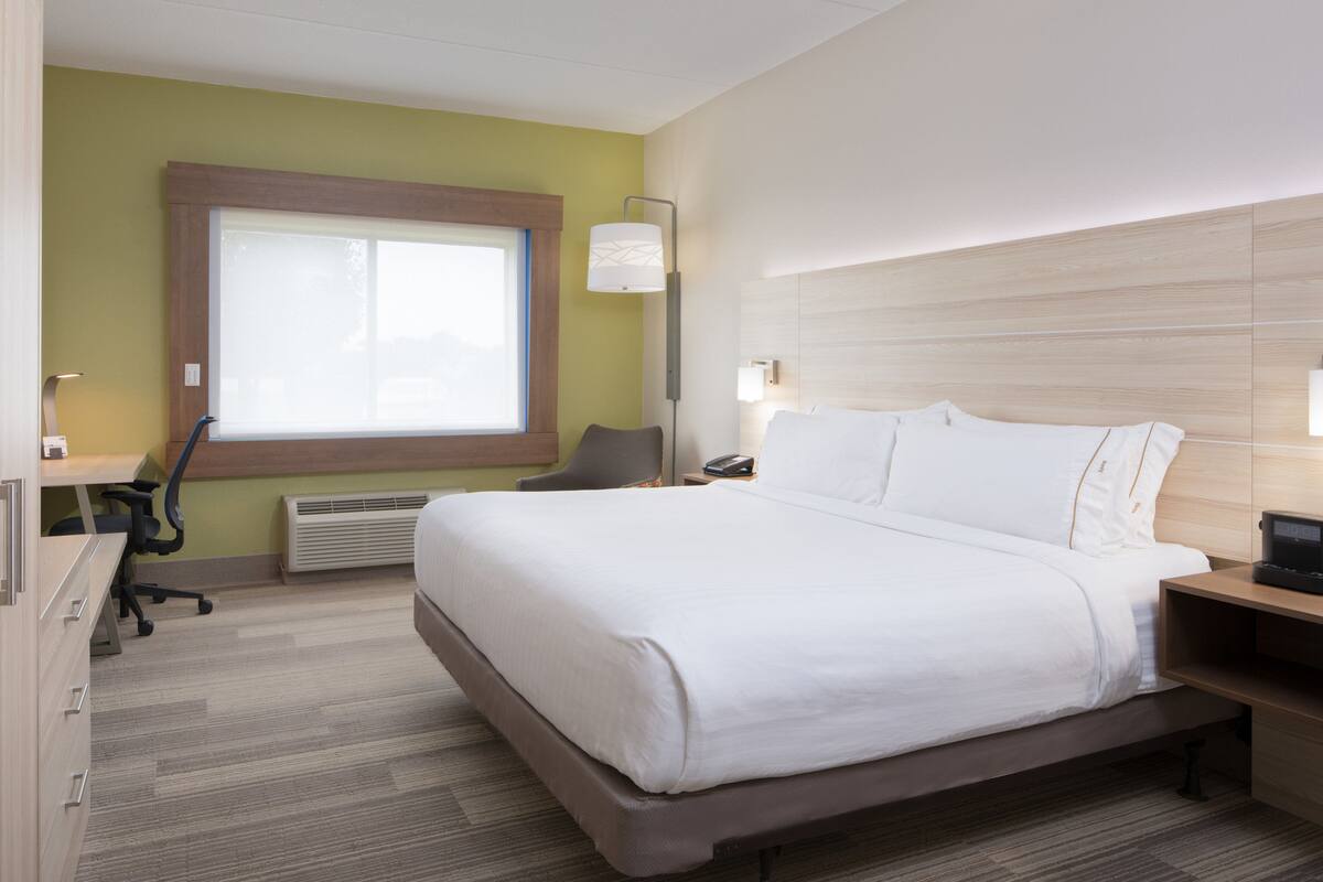 Una camera d'albergo con un letto grande, una scrivania, una sedia, un comodino e una finestra.