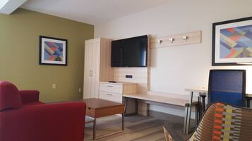 A modern hotel room with a desk, a television, a red armchair, and a framed abstract painting.