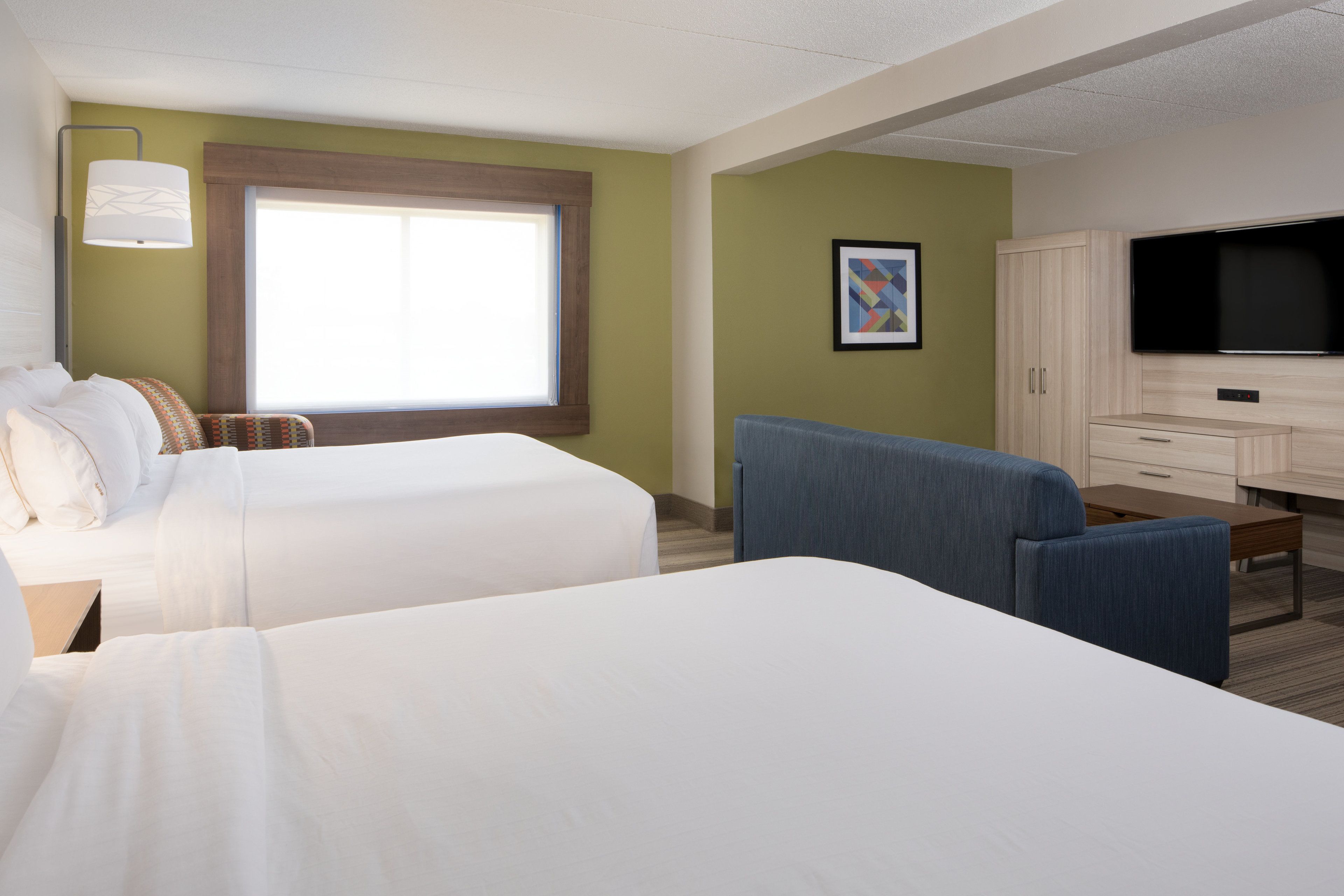A hotel room with two beds, a desk, a chair, a television, and a window.