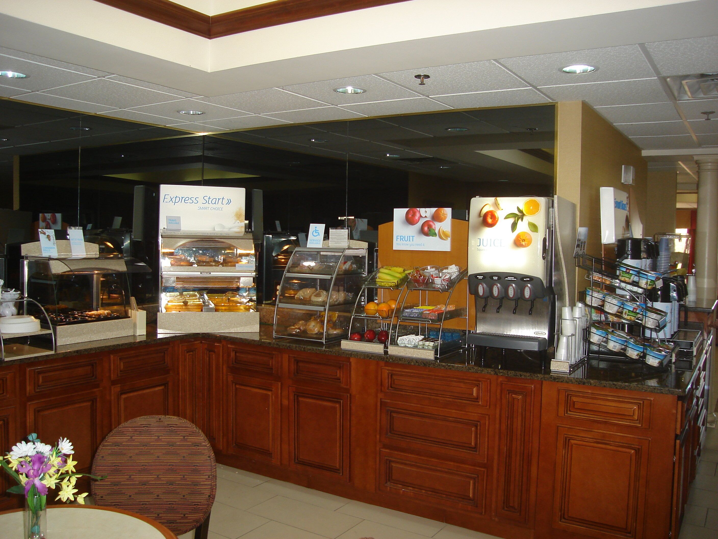 A self-service breakfast station with various food items and a juice dispenser.